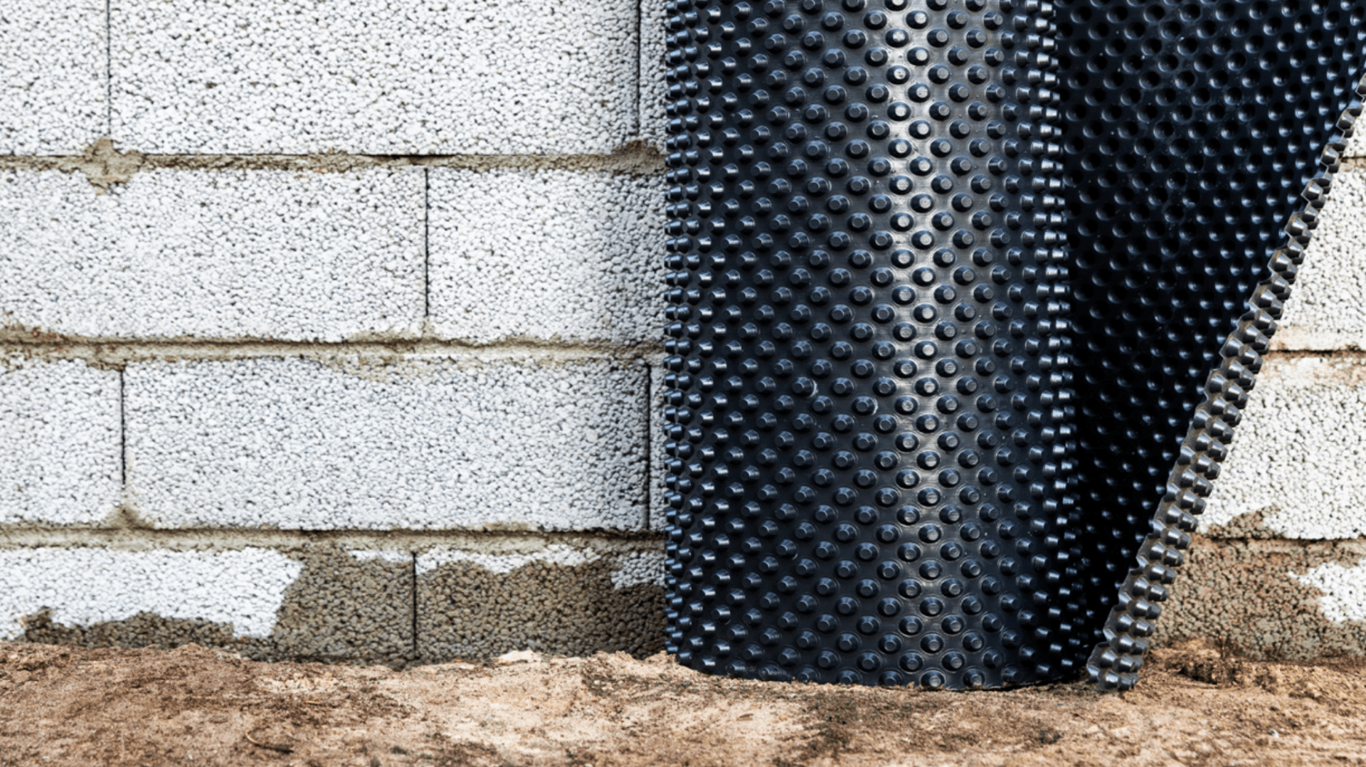 A roll of black foundation waterproofing membrane lays against a brick wall.